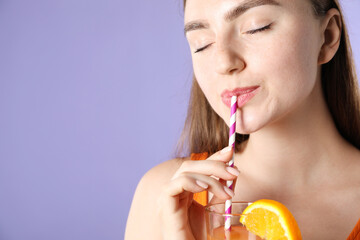 Woman drinking refreshing drink through straw on violet background, space for text