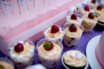 Small dessert cups with layers of cream, sponge cake, marshmallows, and strawberries, decorated for a party.
