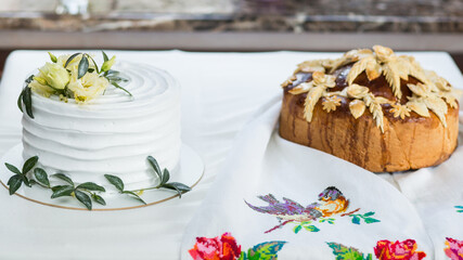 Rustic-style wedding cake with white cream frosting decorated with fresh flowers and greenery, paired with traditional bread loaf. Perfect for natural-themed weddings.
