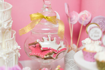 Glass jar filled with crown-shaped cookies decorated with pink and white icing, tied with a golden ribbon, perfect for a princess-themed candy bar.