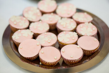 Close-up of pink cupcakes decorated with pastel fondant and delicate white flower patterns, displayed on a silver tray. Sweet party desserts perfect for birthday celebrations, weddings, or festive can
