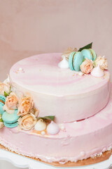 Close-up of a pastel pink cake topped with peach roses, turquoise macarons, and delicate meringues, emphasizing elegant and romantic details.