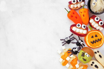 Healthy Halloween fruit and vegetable snacks. Variety of fun, spooky treats. Above view side border over a white marble banner background with copy space.