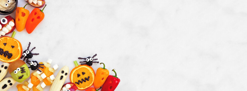 Healthy Halloween fruit and vegetable snacks. Assortment of fun, spooky treats. Overhead view corner border over a white marble banner background with copy space. - Powered by Adobe