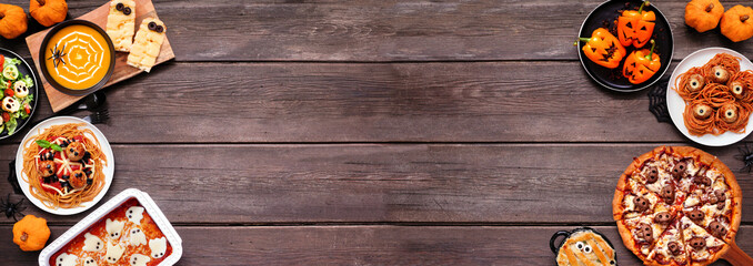 Spooky Halloween dinner party double border over a dark wood banner background. Top view. Skull pizza, salad, pasta, ghost lasagna, mummy pot pie, pumpkin soup, jack o lantern stuffed peppers.
