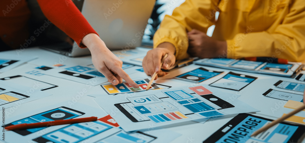 Poster close-up of a collaborative workspace featuring hands selecting user interface mockups from a table.