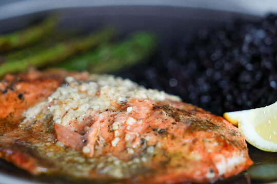 Fresh fish for dinner. Wild caught Coho Salmon fillet topped with garlic butter and served on a plate with black rice and asparagus. Healthy and sustainable food. 