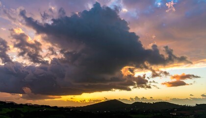 Obraz premium Dramatic sunset sky with vast, dark clouds over a tranquil landscape of hills.