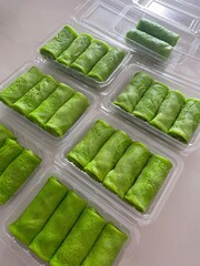 Several containers of green pandan crepes, a sweet Asian dessert, are ready to eat.