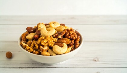 Fototapeta premium A white bowl brimming with a diverse mix of nuts, including almonds, cashews, walnuts, and pecans, sits on a light wooden surface.