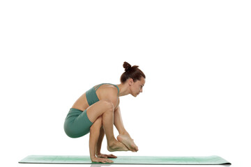 Studio shot of young woman in green outfit practicing firefly preparation yoga pose (bhujapidasana...