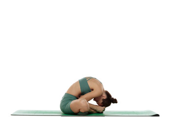 Studio shot of young woman in green outfit practicing bound angle forward bend yoga pose (baddha...