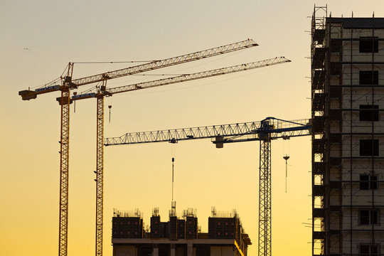 Construction of a new residential area using high-rise cranes at sunset. - Powered by Adobe