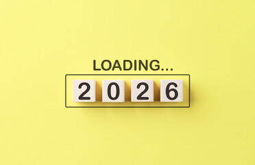 Loading 2026 New Year Progress Concept. Wooden cubes number 2026 inside progress bar with word loading on bright yellow background, symbolizing preparation, progress, goal setting, and upcoming goals.