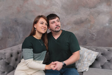 Young happy couple in love hugging against gray wall on gray sofa. husband and wife. bride and groom