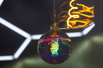 A decorative incandescent light bulb hangs from a dark ceiling.