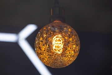 A decorative incandescent light bulb hangs from a dark ceiling.