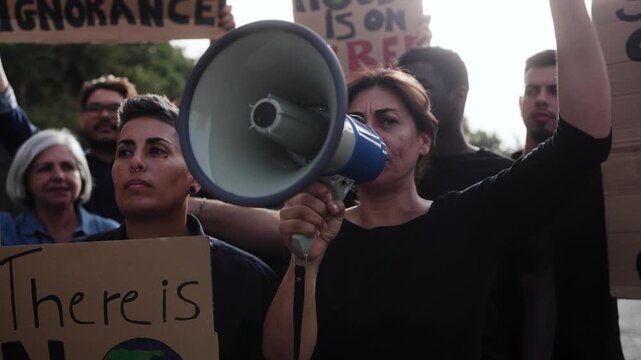Crowd people protesting, woman shouting on megaphone at climate change protest march for environment and social justice