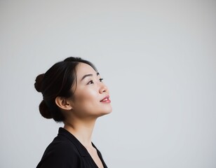 Profile of asian woman with hair in bun looking up against a plain light gray background