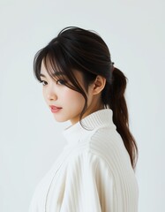 Portrait of a young woman with dark hair in a ponytail wearing a white turtleneck sweater