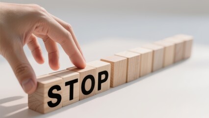 A hand is touching a wooden block with the word stop written on it