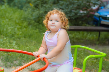 A young child with curly red hair enjoys playing on a brightly colored spinning toy in a lush park....