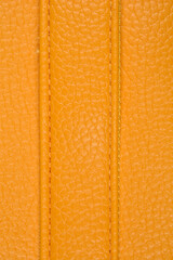 Fototapeta premium A close-up vertical shot of a textured yellow artificial leather surface, featuring two parallel lines of neat, matching-color stitching