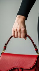 Female hand holding red leather handbag with brass accents