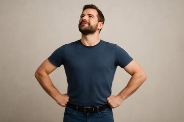Portrait of a confident young man standing with arms akimbo and looking up against a plain background