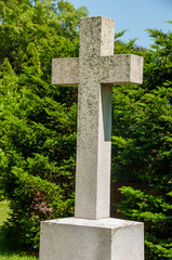 Stone cross monument stands amidst lush green vegetation creating a serene scene symbolizing tranquility and faith.