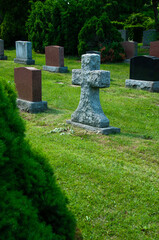 Tranquil graveyard featuring a stone cross and multiple headstones surrounded by lush greenery...