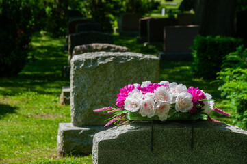 A peaceful cemetery scene featuring gravestones adorned with beautiful flowers, surrounded by lush...