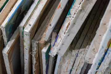 Stack of mixed old and new paintings canvases stored vertically in artist studio collection
