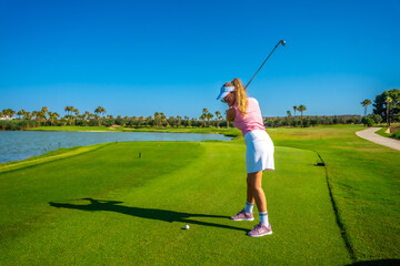 Female golfer putting on green with lake in background on sunny day