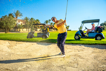 Golfer playing from sand trap on sunny day with golf cart © unai