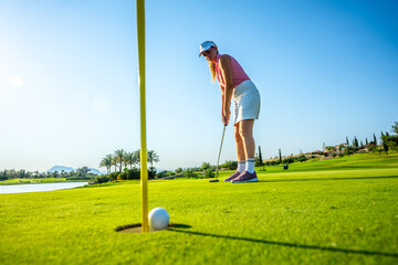 Female golfer putting on sunny golf course