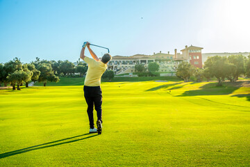 Golfer swinging golf club on lush green course at luxury resort