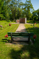 A tranquil cemetery scene featuring a bench, memorial flowers, and a columbarium in a verdant setting, surrounded by greenery and sunlight creating a peaceful and serene atmosphere.
