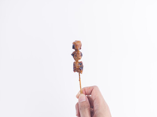 Hand holding spicy grilled meatball skewer with peanut sauce on white background. Isolated Asian...