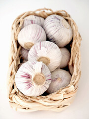 A small basket is filled with several heads of garlic. The garlic bulbs have white skins with...