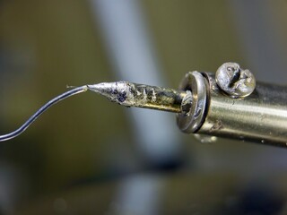 close-up of a soldering iron tip with melted solder and a wire attached, showing the industrial...