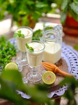 Sweet Lacchi Drinko, Two elegant glasses filled with a refreshing, creamy beverage, garnished with fresh mint leaves, alongside a vintage-style jug and half a lime.