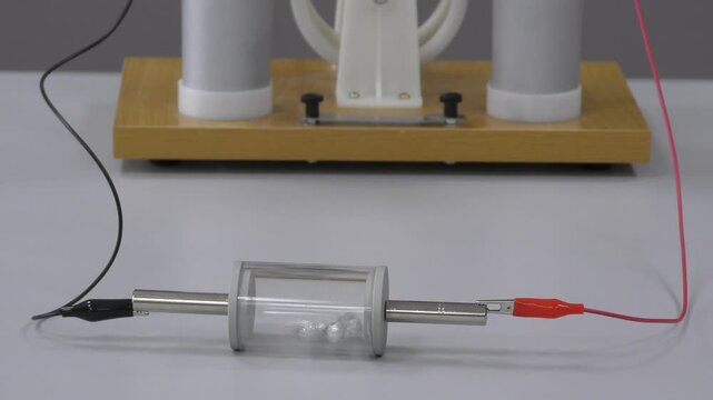 Physics demonstration of electrostatics experiment showing the transfer of electric charge between objects. Teacher explains principles of static electricity to students during a classroom lesson.