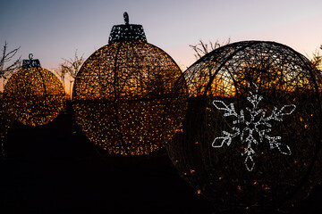 Decorative holiday ornaments illuminated at sunset among trees in a festive display