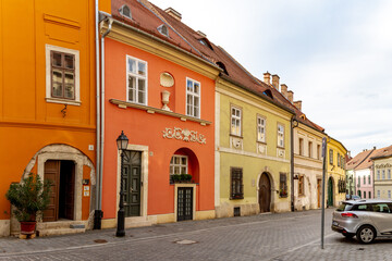 Obraz premium Quaint curved street in Buda Castle District Old Town with pastel Baroque and Classicism houses, vintage lanterns, and cobblestones, showcasing historic charm beyond tourist paths. Budapest, Hungary. 