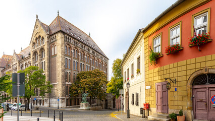 View of Vienna Gate Square from curved Buda Old Town street with pastel houses, featuring National...