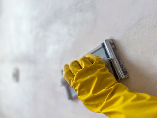 Construction worker sanding wall with hand sander wearing yellow gloves