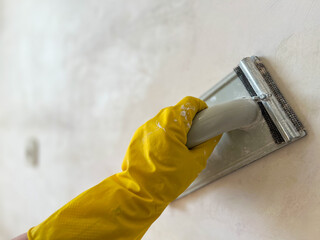 Construction worker sanding wall with sandpaper tool wearing yellow gloves