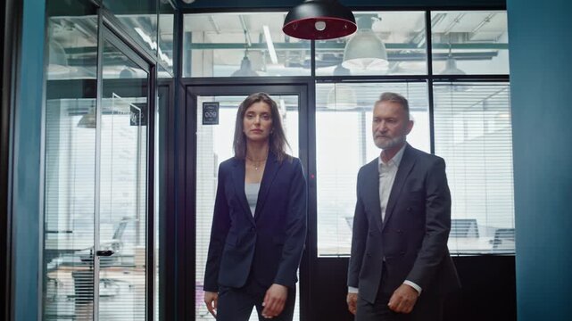 Two colleagues walking office hall in elegant suits closeup. Serious partners
