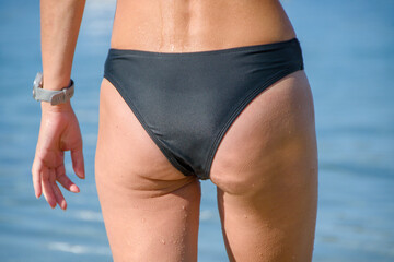 female ass in black wet swimsuit close-up against sea background
